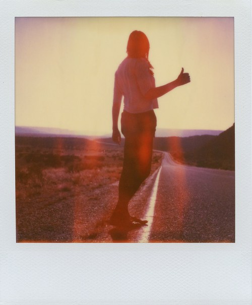 Silhouette of a person giving a thumbs up on a deserted road at sunset, with a warm, vintage filter effect.