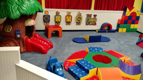 Colorful indoor play area with a treehouse slide, soft play structures, and a train-themed wall decoration.