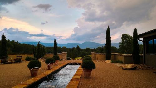 Scenic view of a landscaped garden with a water feature, mountains in the background, and cloudy skies.
