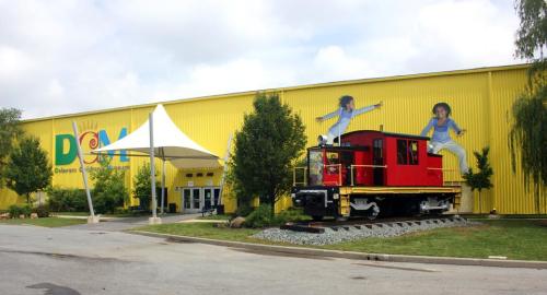 Bright yellow building with a red train on display outside, featuring colorful murals of children playing.