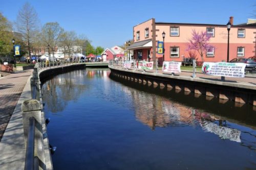 A peaceful canal lined with trees and buildings, reflecting a clear blue sky on a sunny day.