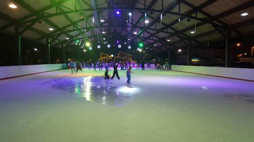 A lively indoor ice skating rink with colorful lights and people skating, surrounded by festive decorations.