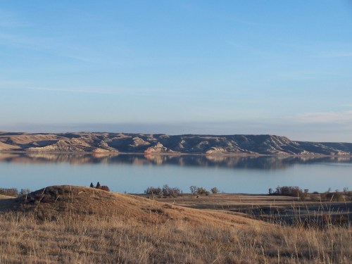 A serene landscape featuring a calm lake reflecting hills under a clear blue sky, surrounded by grassy terrain.