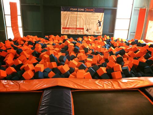A colorful foam pit filled with orange and blue blocks, surrounded by safety padding in a trampoline park.