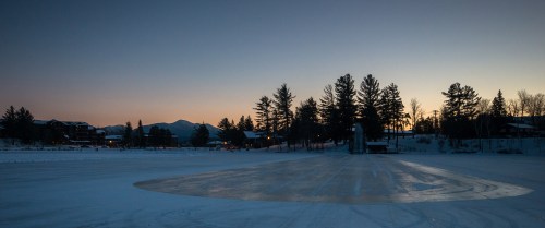 A serene winter landscape at dusk, featuring a frozen lake, trees, and a soft gradient sky.