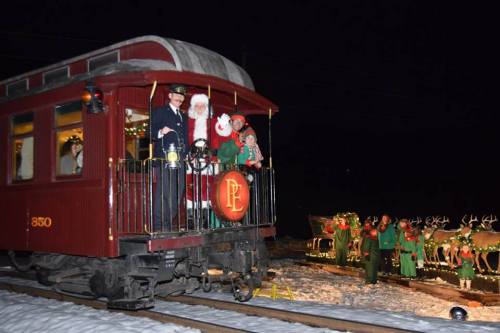 A festive train with Santa, a child, and a conductor, surrounded by decorated cars in a snowy night setting.