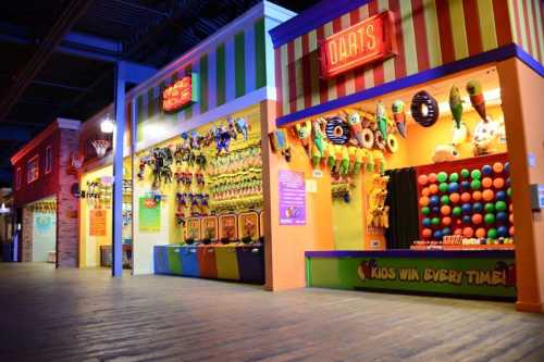 Colorful arcade game booths with various prizes, including darts and colorful balls, in a vibrant indoor setting.