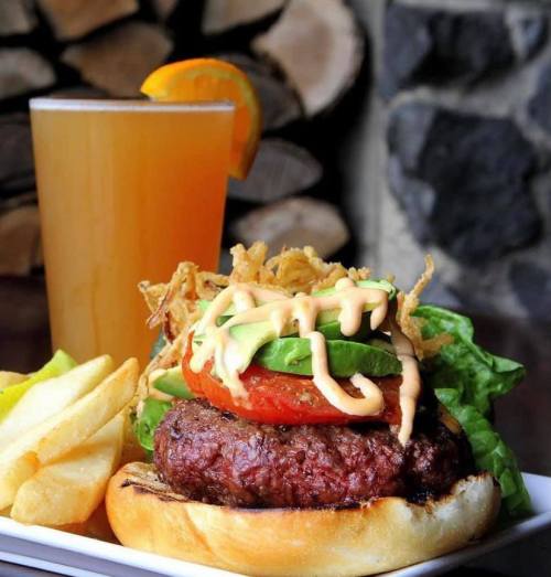 A juicy burger with lettuce, tomato, and sauce, served with fries and a glass of beer garnished with an orange slice.