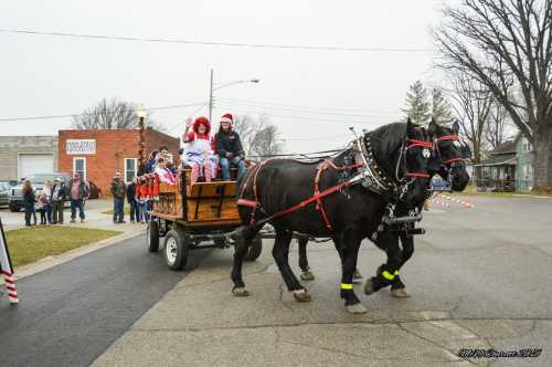 A horse-drawn wagon with festive passengers rides through a small town during a holiday event.