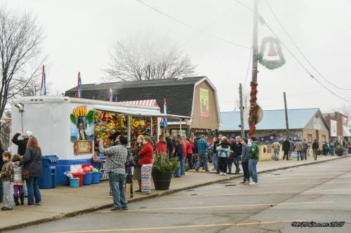 A bustling street fair scene with people gathered around food stalls and festive decorations on a foggy day.
