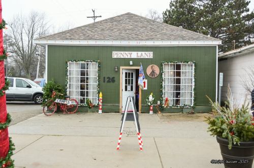 A green building with a sign reading "Penny Lane," decorated for the holidays, featuring festive wreaths and a welcoming entrance.