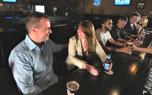 A group of friends enjoying drinks at a bar, smiling and chatting at a long wooden counter.