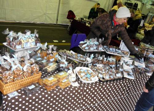 A vendor arranges a variety of baked goods on a table covered with a polka dot tablecloth at a market.