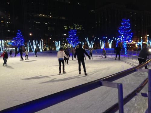 People ice skating at night, surrounded by trees adorned with blue lights.