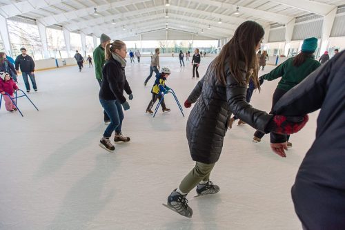 A group of people ice skating indoors, some using skating aids, in a lively rink setting.