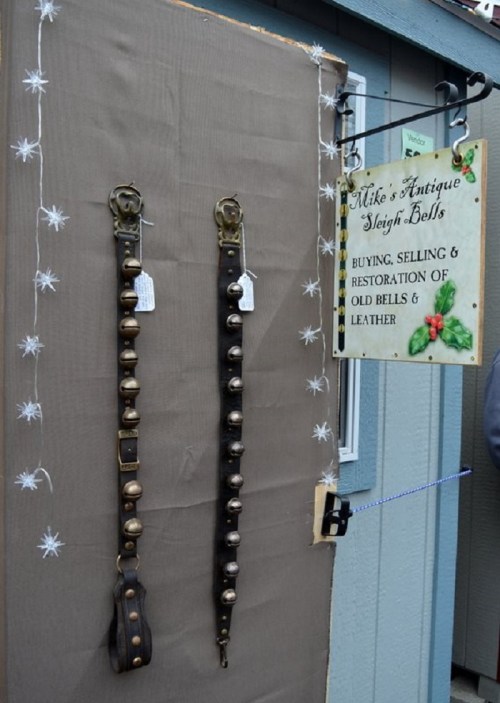Two antique sleigh bell straps hang on a wall next to a sign for "Mike's Antique Sleigh Bells" shop.