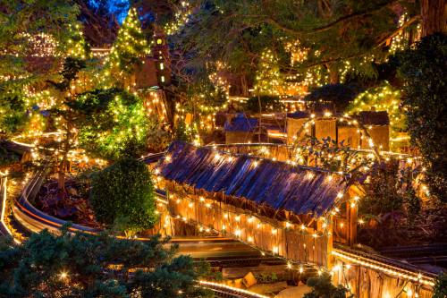 A beautifully lit miniature village with twinkling lights and winding tracks, set in a lush, green landscape at night.