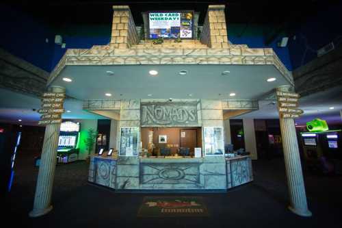 Entrance of a gaming center named "Nomads," featuring a stone-like design and digital screens displaying promotions.