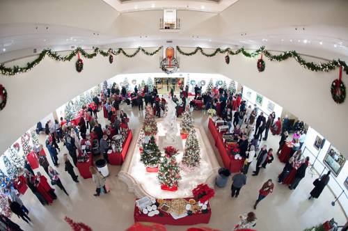 A festive indoor event with decorated Christmas trees, guests mingling, and holiday decorations throughout the space.