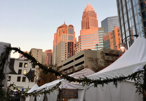 City skyline at sunset with holiday tents in the foreground, adorned with festive decorations.