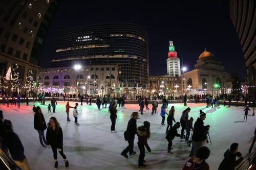 A bustling ice skating rink at night, surrounded by festive lights and buildings, with skaters enjoying the scene.
