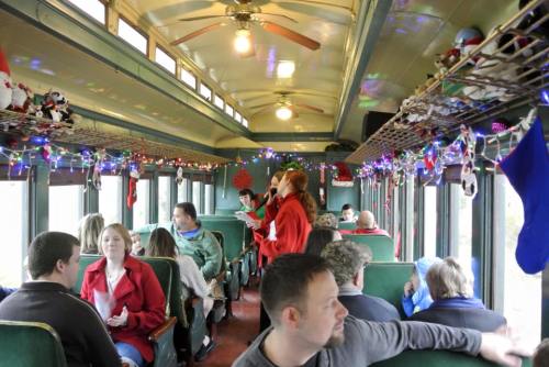 A festive train interior decorated with lights and stockings, filled with passengers enjoying the holiday atmosphere.