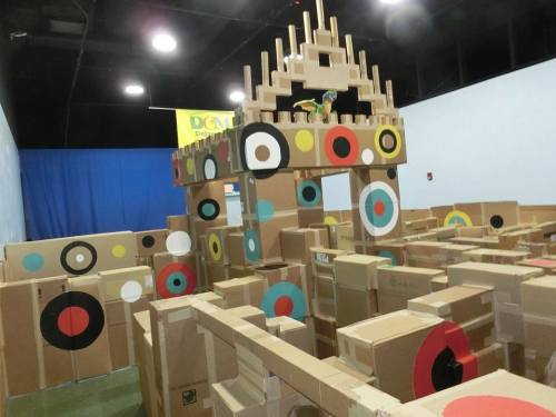 A colorful cardboard structure with targets, resembling a castle, in a spacious indoor area.
