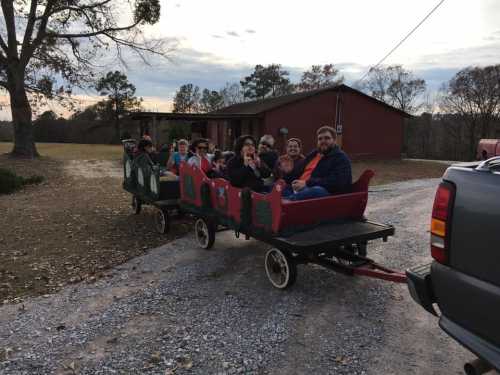 A group of people sitting in a festive wagon on a gravel path, with a house and trees in the background.