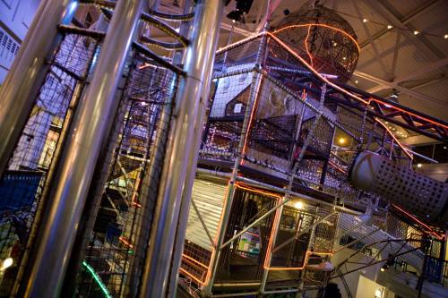 A colorful indoor play structure with metal frames and lights, featuring tunnels and climbing areas.