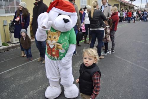 A child stands next to a polar bear mascot in a Santa hat, with a festive crowd in the background.