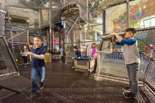 Children play in a colorful indoor playground with climbing structures and interactive features.