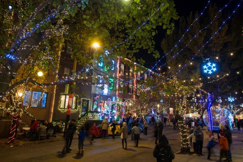 A festive street scene at night, adorned with colorful Christmas lights and decorations, with people enjoying the atmosphere.