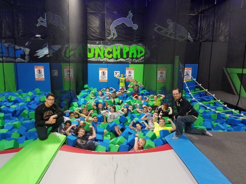 A group of children and adults posing in a foam pit at a trampoline park, smiling and flexing their muscles.