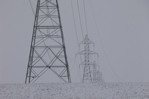 Snow-covered landscape with tall power lines and towers against a gray sky.