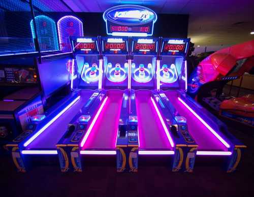 A brightly lit arcade with four skee-ball machines, featuring neon lights and score displays.