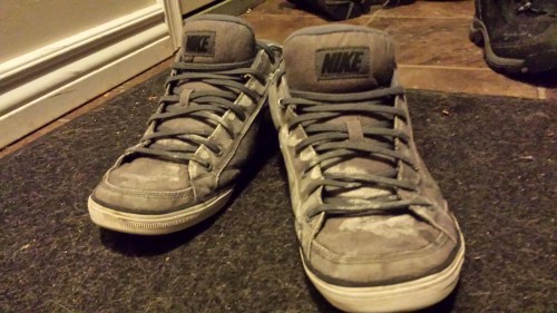Worn Nike sneakers with scuffed surfaces, resting on a dark mat near a doorway.