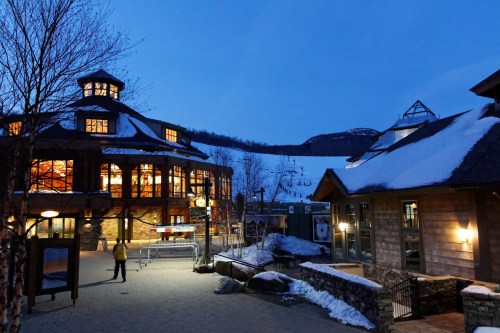 A snowy landscape at dusk, featuring a cozy lodge with warm lights and a mountain backdrop.