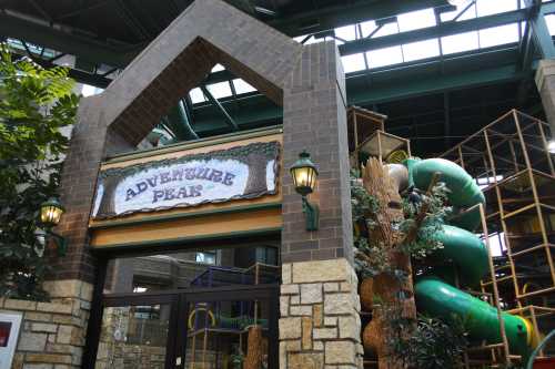 Entrance to "Adventure Peak," featuring a large green slide and play structure in a spacious indoor setting.