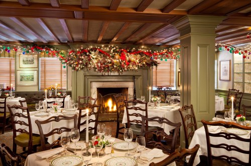 Cozy restaurant interior decorated for the holidays, featuring tables, a fireplace, and festive garlands.