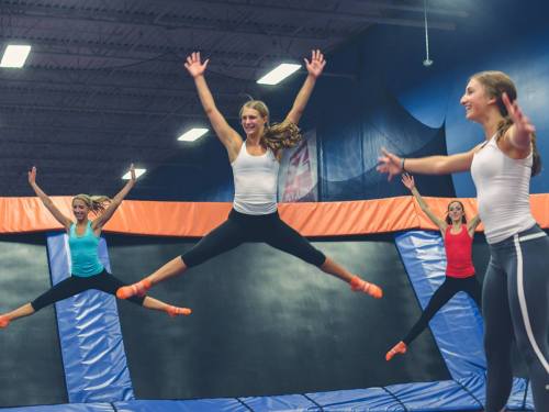 Four women jumping on trampolines in a trampoline park, smiling and enjoying their time.
