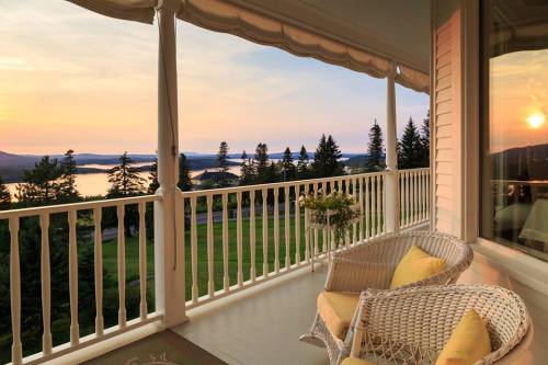 A serene balcony view at sunset, overlooking a lake and trees, with two wicker chairs and yellow cushions.