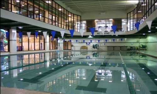 Indoor swimming pool with clear water, blue and white flags, and large windows overlooking the area.