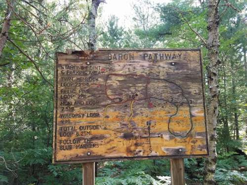 Trail map sign for Baron Pathway, detailing loop trails and distances in a wooded area. Follow blue markers.