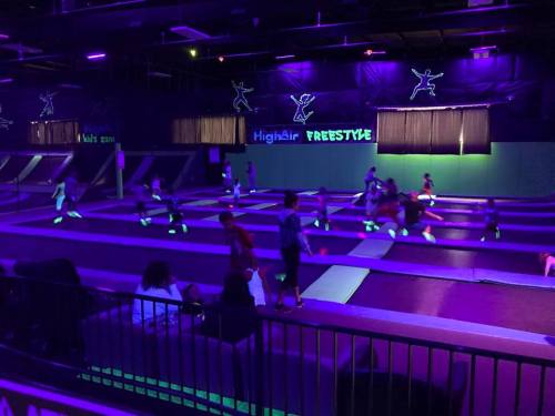 A vibrant indoor trampoline park with kids jumping under neon lights and a dark atmosphere.