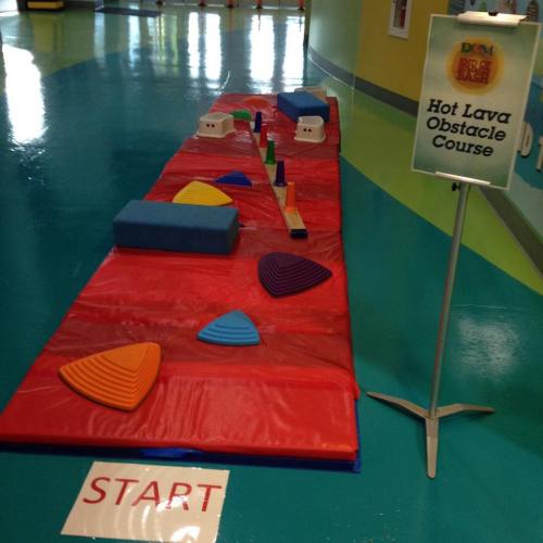 Colorful indoor obstacle course with foam shapes on a red mat, marked with a "START" sign and a "Hot Lava Obstacle Course" sign.