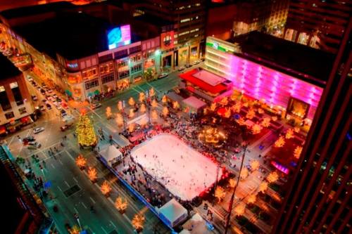 Aerial view of a vibrant ice skating rink surrounded by festive lights and holiday decorations in a city square.