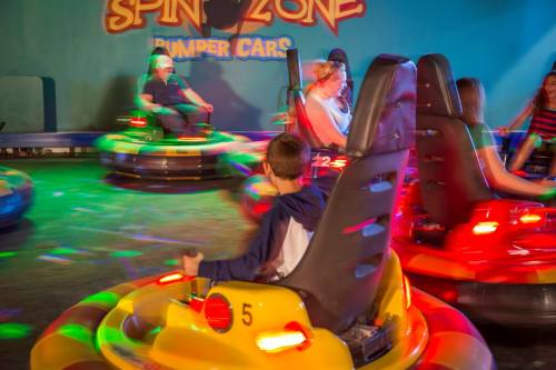 A colorful indoor bumper car arena with people enjoying rides amidst vibrant lights and motion.