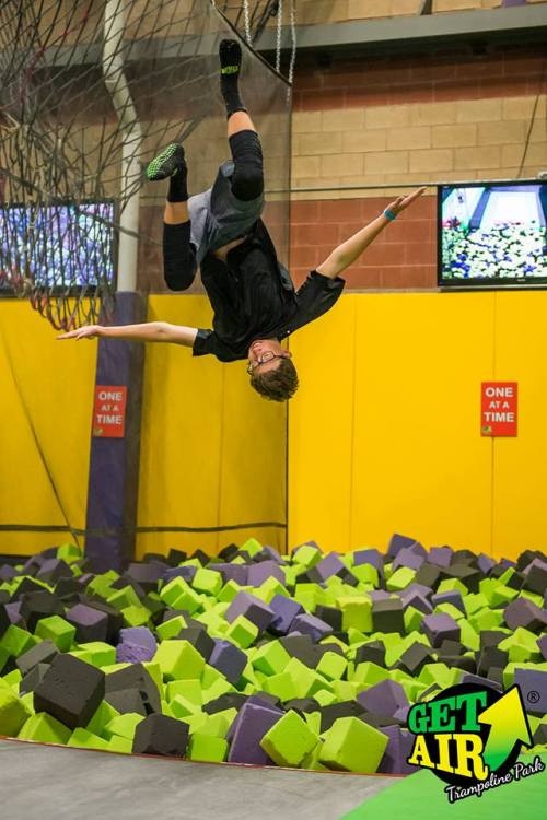 A person performs a flip in mid-air above a colorful foam pit at a trampoline park.