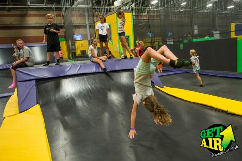 A lively trampoline park scene with kids jumping, flipping, and playing on trampolines and foam pits.