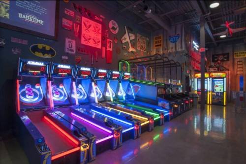 A vibrant arcade with neon-lit skee-ball machines and various games lining the walls.
